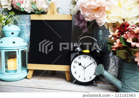 Easel mockup with blue landtern, alarm clock and flowers bouquet decoration on wooden background 111181863