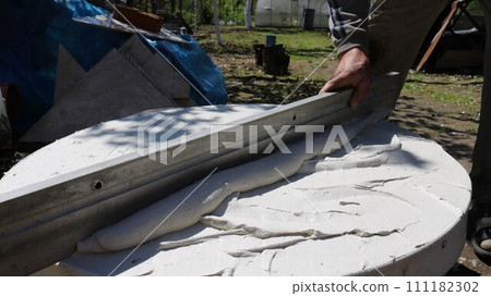 applying and leveling a layer of soft finishing mortar on a flat round surface using a long flat beam in the process of making homemade furniture, preparing the tabletop for tiling applying and leveling a layer of soft finishing mortar on a flat round surface using a long flat beam in the process of making homemade furniture, preparing the tabletop for tiling 111182302