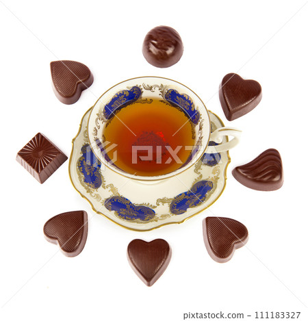 Tea in a porcelain vintage cup and chocolates isolated on a white. Tea in a porcelain vintage cup and chocolates isolated on a white. 111183327