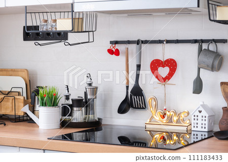 The interior of the kitchen in the house is decorated with red hearts for Valentine's Day. Decor on the table, stove, utensils, festive mood in a family nest 111183433
