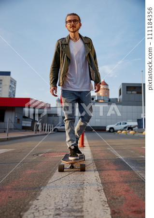 Hipster guy riding skateboard prefers eco-friendly transportation among city Hipster guy riding skateboard prefers eco-friendly transportation among city 111184356