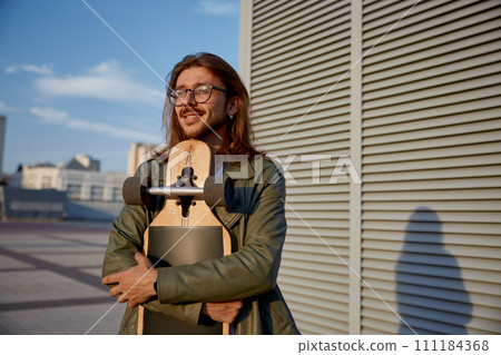 Thoughtful hipster guy holding skateboard dreaming and looking at sunset Thoughtful hipster guy holding skateboard dreaming and looking at sunset 111184368