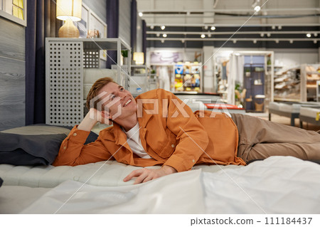 Handsome happy guy examining orthopedic mattress on sale at shop 111184437