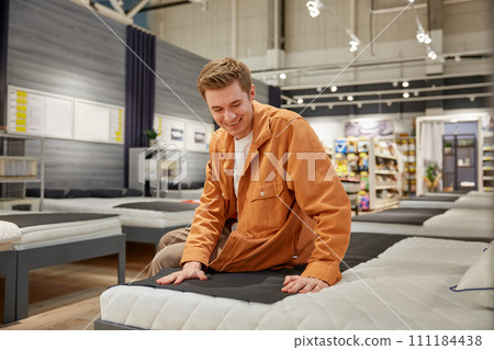 Handsome male customer sitting on new bed at furniture store 111184438