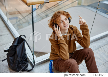 Teenager boy relaxing at shopping mall sitting on floor listening music 111184470