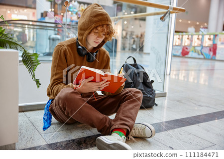 Teenage boy writing in notebook while sitting on floor of shopping mall Teenage boy writing in notebook while sitting on floor of shopping mall 111184471