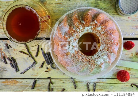 Old fashioned sand cake with cup of black tea and pieces of vanilla on wooden background. Egg-yolk sponge cake with stawberries on rustic white background 111184884