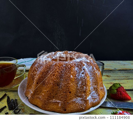 Old fashioned sand cake with cup of black tea and pieces of vanilla on wooden background. Egg-yolk sponge cake on rustic white background. Pouring sugar on sand cake Old fashioned sand cake with cup of black tea and pieces of vanilla on wooden background. Egg-yolk sponge cake on rustic white background. Pouring sugar on sand cake 111184908