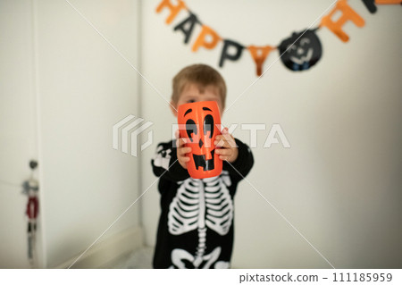 Boy in a skeleton costume and a pumpkin in his hands 111185959