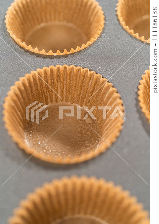 Getting ready to bake delicious chocolate cupcakes, we carefully line the cupcake pan with paper liners, ensuring a delightful treat awaits. 111186138