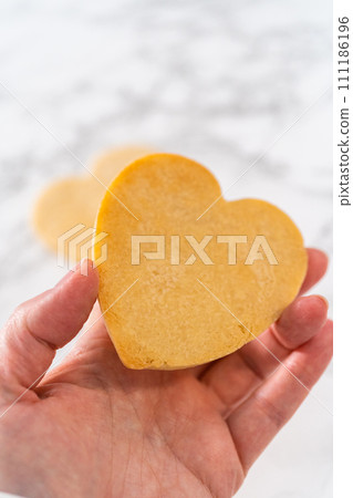 Decorating heart-shaped sugar cookies with pink and white royal icing for Valentine's Day. Decorating heart-shaped sugar cookies with pink and white royal icing for Valentine's Day. 111186196