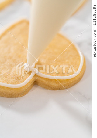 Decorating heart-shaped sugar cookies with pink and white royal icing for Valentine's Day. Decorating heart-shaped sugar cookies with pink and white royal icing for Valentine's Day. 111186198