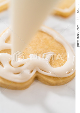 Decorating heart-shaped sugar cookies with pink and white royal icing for Valentine's Day. Decorating heart-shaped sugar cookies with pink and white royal icing for Valentine's Day. 111186209