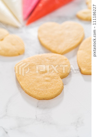 Decorating heart-shaped sugar cookies with pink and white royal icing for Valentine's Day. Decorating heart-shaped sugar cookies with pink and white royal icing for Valentine's Day. 111186227