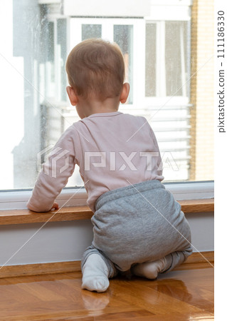 Baby gazes longingly through window, eager for an outdoor adventure. Concept of longing and childhood curiosity Baby gazes longingly through window, eager for an outdoor adventure. Concept of longing and childhood curiosity 111186330