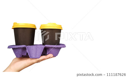 Female hand holding and serving two disposable cups of coffee on a white background with copy space in the studio. Breakfast on the go. Paper glasses with hot drinks in black and yellow plastic lids 111187626