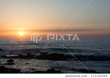 在地平線和多岩石的海岸上的日落 111193449