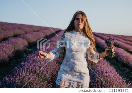 Woman lavender field. Happy carefree woman in a white dress walking in a lavender field and smelling a lavender bouquet on sunset. Ideal for warm and inspirational concepts in wanderlust and travel. 111195871