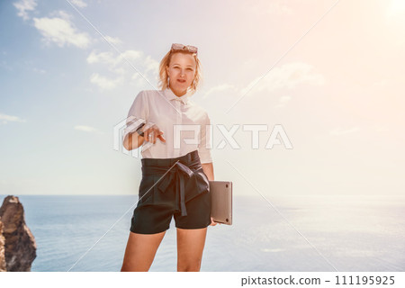 Digital nomad, Business woman working on laptop by the sea. Pretty lady typing on computer by the sea at sunset, makes a business transaction online from a distance. Freelance, remote work on vacation Digital nomad, Business woman working on laptop by the sea. Pretty lady typing on computer by the sea at sunset, makes a business transaction online from a distance. Freelance, remote work on vacation 111195925