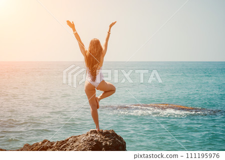 Woman sea yoga. Back view of free calm happy satisfied woman with long hair standing on top rock with yoga position against of sky by the sea. Healthy lifestyle outdoors in nature, fitness concept. 111195976