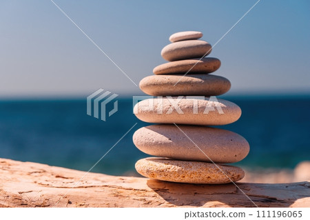 Balanced pebble pyramid on the beach on a sunny day. Abstract Sea bokeh on the background. Selective focus. Zen stones on the sea beach, meditation, spa, harmony, calmness, balance concept 111196065