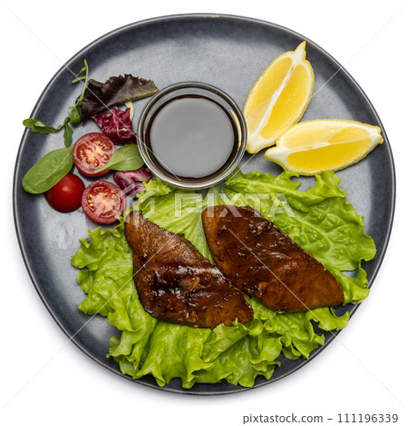 pieces of Organic grilled Tuna Steak on black ceramic serving dish with salad on a table 111196339