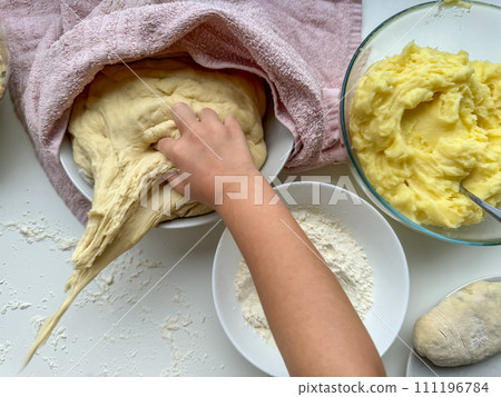 The hands of child knead the dough for making pies on white table, top view. The hands of child knead the dough for making pies on white table, top view. 111196784