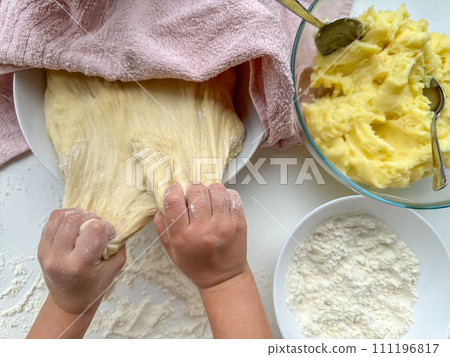 The hands of child knead the dough for making pies on white table, top view. 111196817