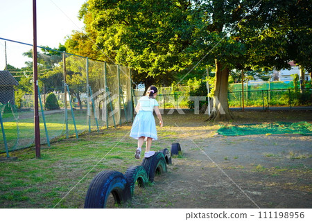 A fourth grade elementary school girl is playing with tire play equipment in the park. 111198956