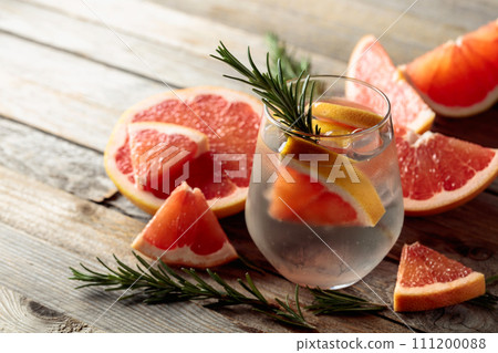 Gin tonic with ice, rosemary, and grapefruit slices on an old wooden table. 111200088