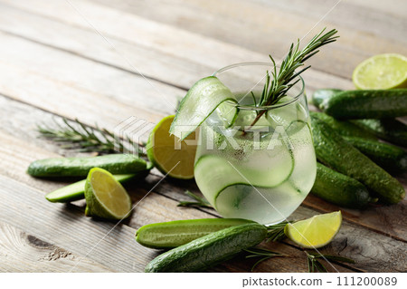 Gin tonic with ice, rosemary, lime, and cucumber on an old wooden table. 111200089