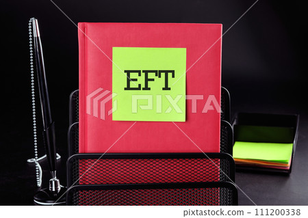 EFT Text on a yellow sticker on a red vertical notepad on a black background next to a pen and money EFT Text on a yellow sticker on a red vertical notepad on a black background next to a pen and money 111200338