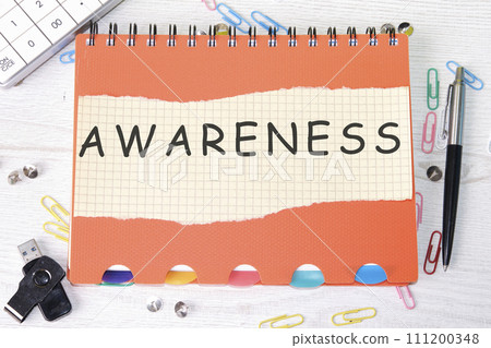 AWARENESS word is written on a sheet in a cage lying on a notebook on the table next to stationery 111200348