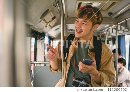 Smiling Asian man with backpack standing in bus and traveling with public transport 111200502