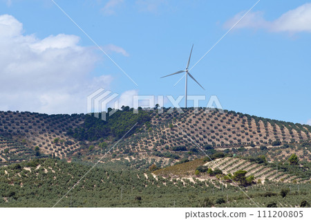 Green energy wind park with rotating high wind turbines for generation electricity, on high mountains among olive groves, over blue cloudy sky background. Green ecological power energy generation. Green energy wind park with rotating high wind turbines for generation electricity, on high mountains among olive groves, over blue cloudy sky background. Green ecological power energy generation. 111200805