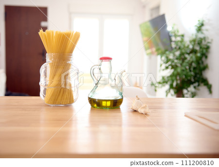Front shot of a glass vintage bottle of fresh extra virgin olive oil and Italian spaghetti on the table in the home kitchen. Food and drink. Healthy organic food. Copy advertising space. Still life 111200810