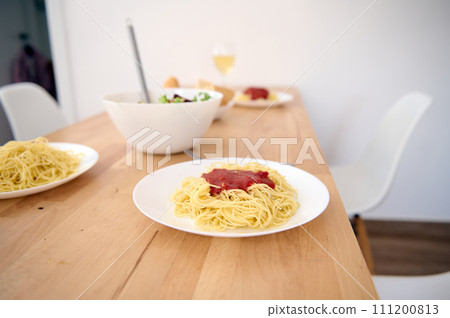 A wooden table with served dishes of freshly prepared Spaghetti with tomato sauce in modern light home kitchen interior. Food and drink concept. Healthy eating and dieting. Italian traditional cuisine A wooden table with served dishes of freshly prepared Spaghetti with tomato sauce in modern light home kitchen interior. Food and drink concept. Healthy eating and dieting. Italian traditional cuisine 111200813