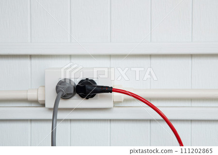 An electric plug with a gray and red cable in the socket. 111202865