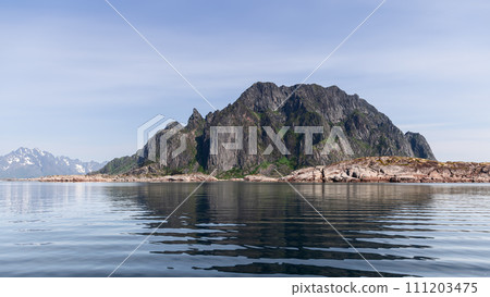 A serene panorama of the rugged Lofoten Islands in Norway, where jagged peaks pierce the sky 111203475