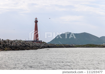 A towering red lighthouse of Andenes stands guard on a rocky shore. Lofoten Islands, Norway 111203477
