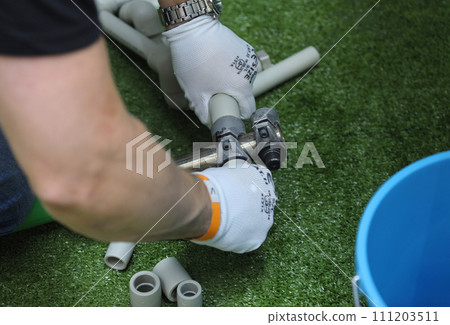 Plumber hands in gloves joining plastic pipes with the soldering iron for PVC pipes 111203511