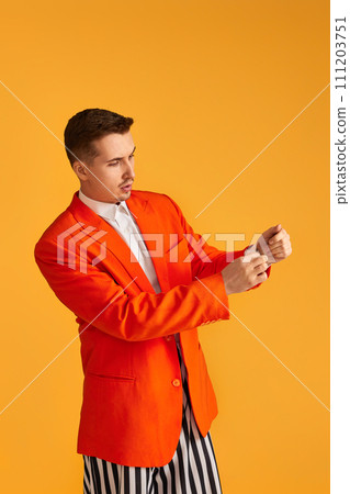 Cheerful funny young man in orange jacket and striped pants on yellow background. 111203751