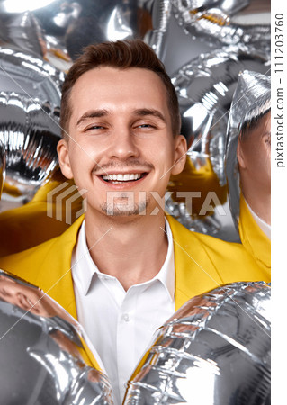 portrait of happy man in yellow jacket with a lot of silver air balloons. birthday party 111203760