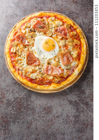 Italian Pizza Bismarck topped with tomato sauce, melted cheese, egg, mushrooms, ham close-up on a wooden board. Vertical top view 111203853
