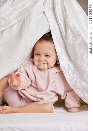 cute funny little child girl looks out from under the blanket on the bed cute funny little child girl looks out from under the blanket on the bed 111203976
