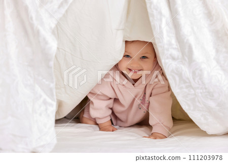 cute funny little child girl looks out from under the blanket on the bed, copy space cute funny little child girl looks out from under the blanket on the bed, copy space 111203978