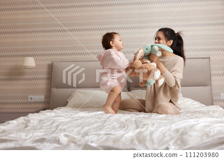 happy mother and her little child daughter playing with bunny toys in bedroom, family having fun happy mother and her little child daughter playing with bunny toys in bedroom, family having fun 111203980