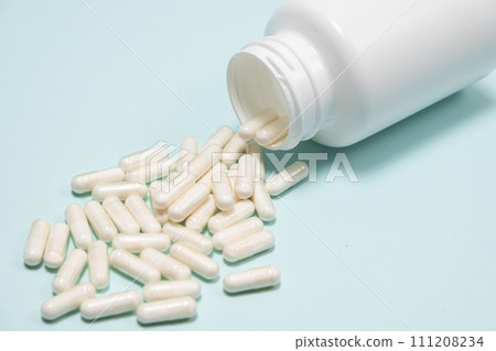White medicine capsules spilled out of a jar on light blue background close-up. 111208234