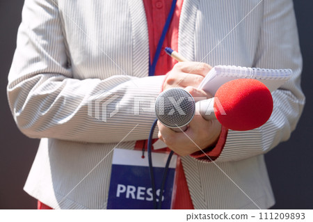 Female journalist at news conference, writing notes, holding microphone Female journalist at news conference, writing notes, holding microphone 111209893