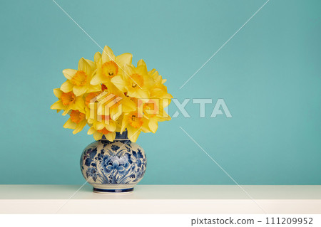 Bouquet of daffodil flowers in a delft blue vase on a blue background 111209952